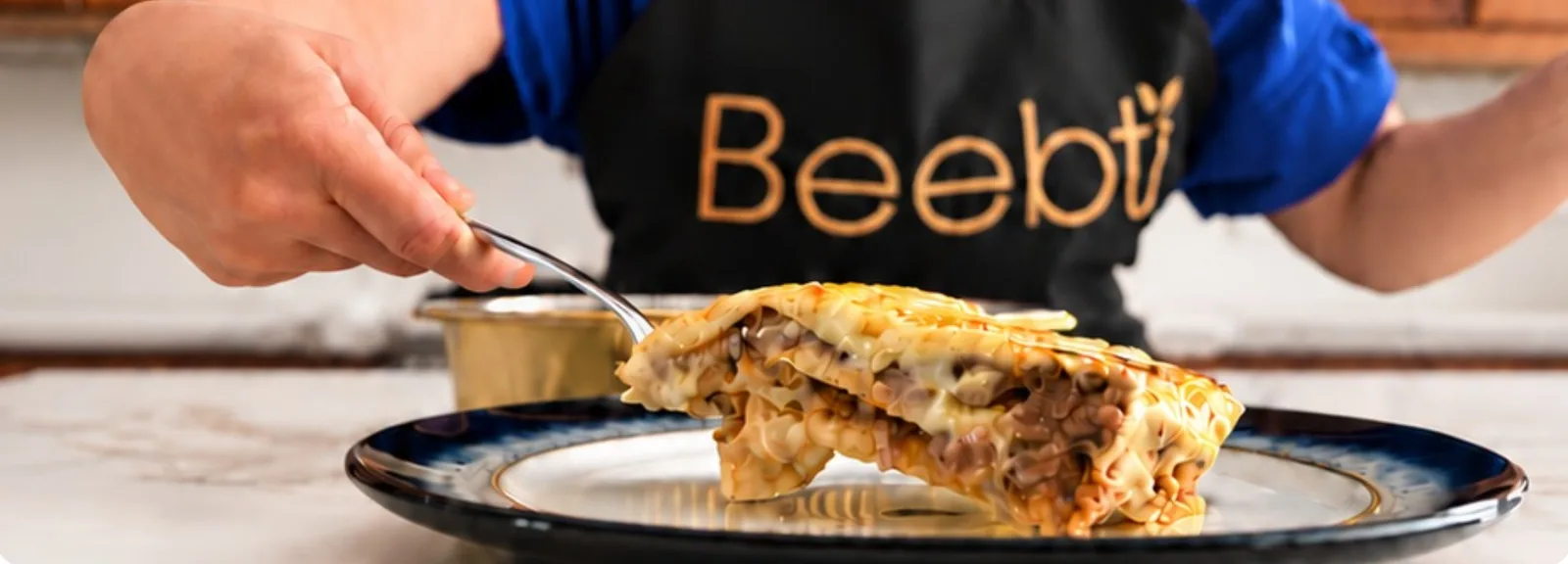 Angie, in her Beebti apron, serving a slice of beef béchamel lasagna onto a plate